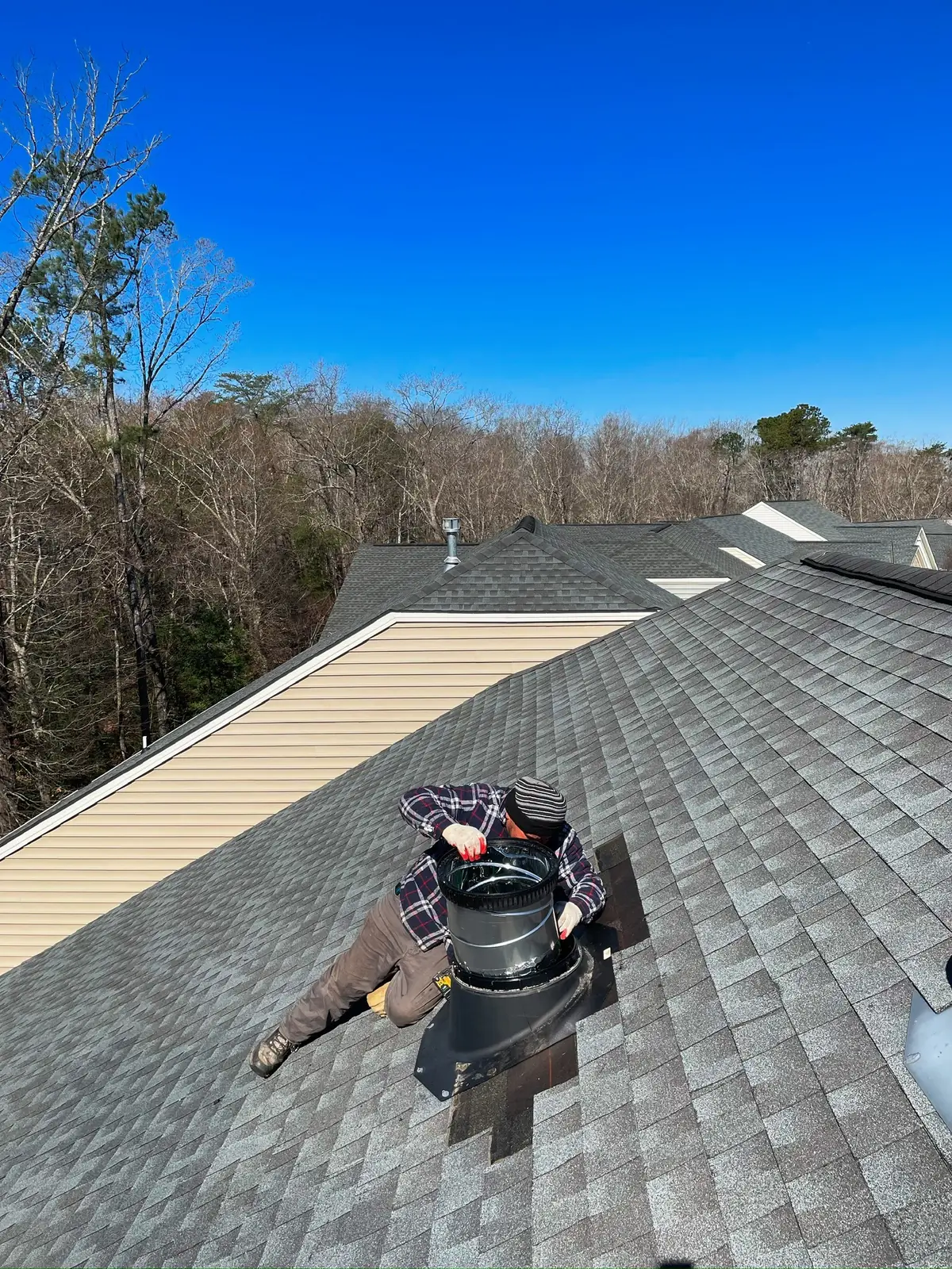 Pipe boot and vent flashing on a gray architectural shingle roof, with a roofer's tools nearby