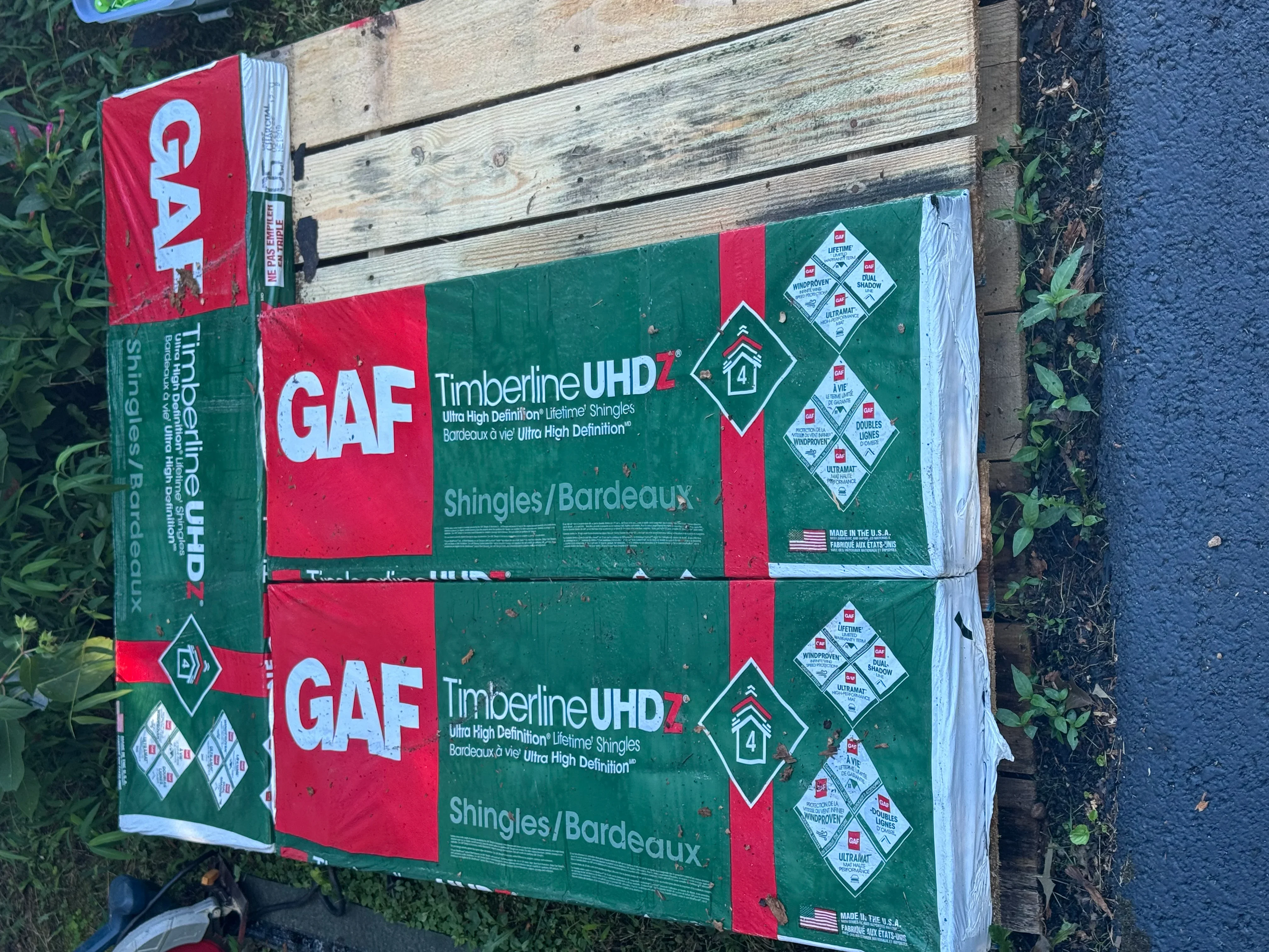 Stacked bundles of GAF Timberline UHD asphalt shingles with green and red packaging