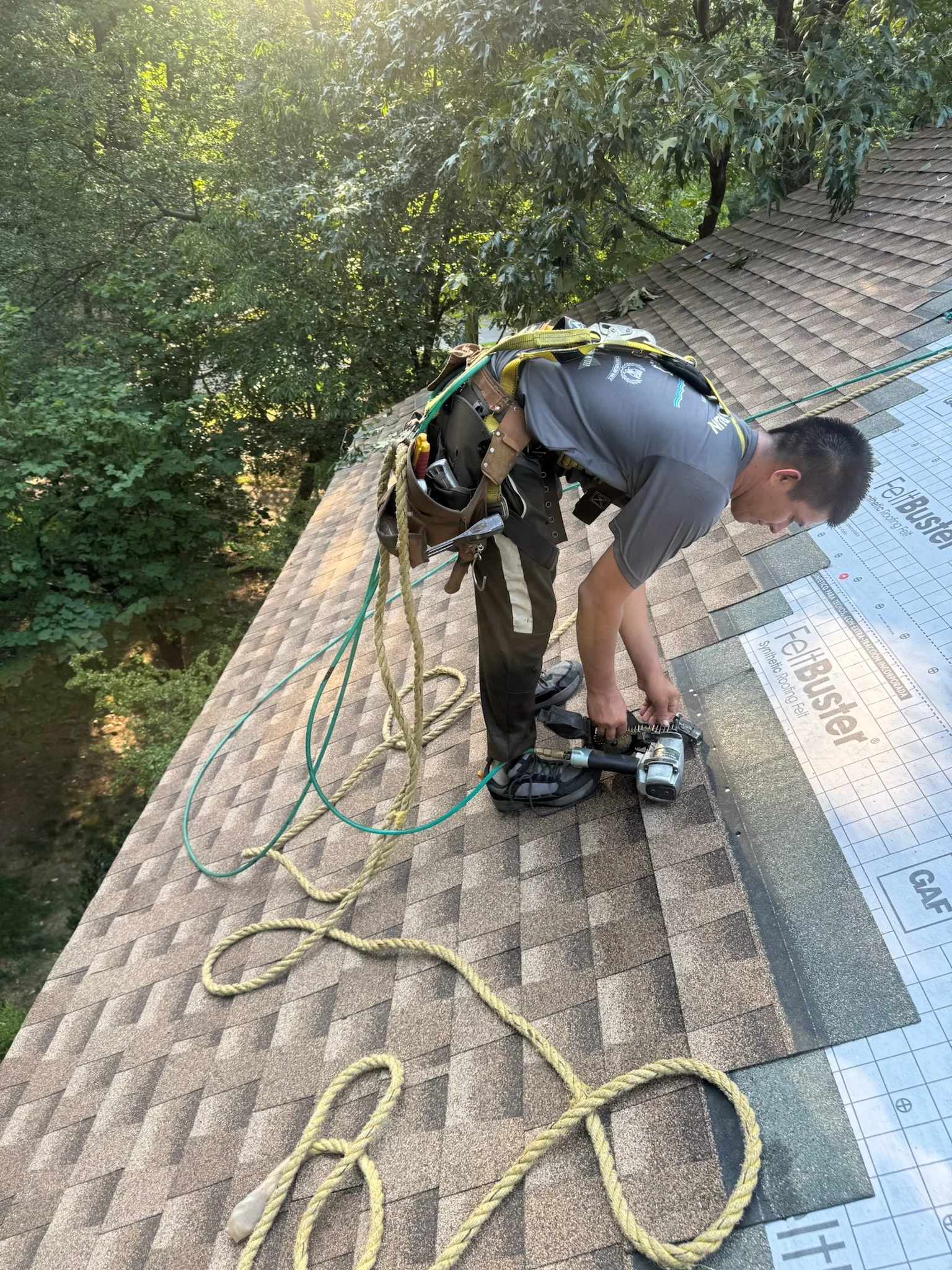 Technician performing roof inspection with safety harness on asphalt shingle roof