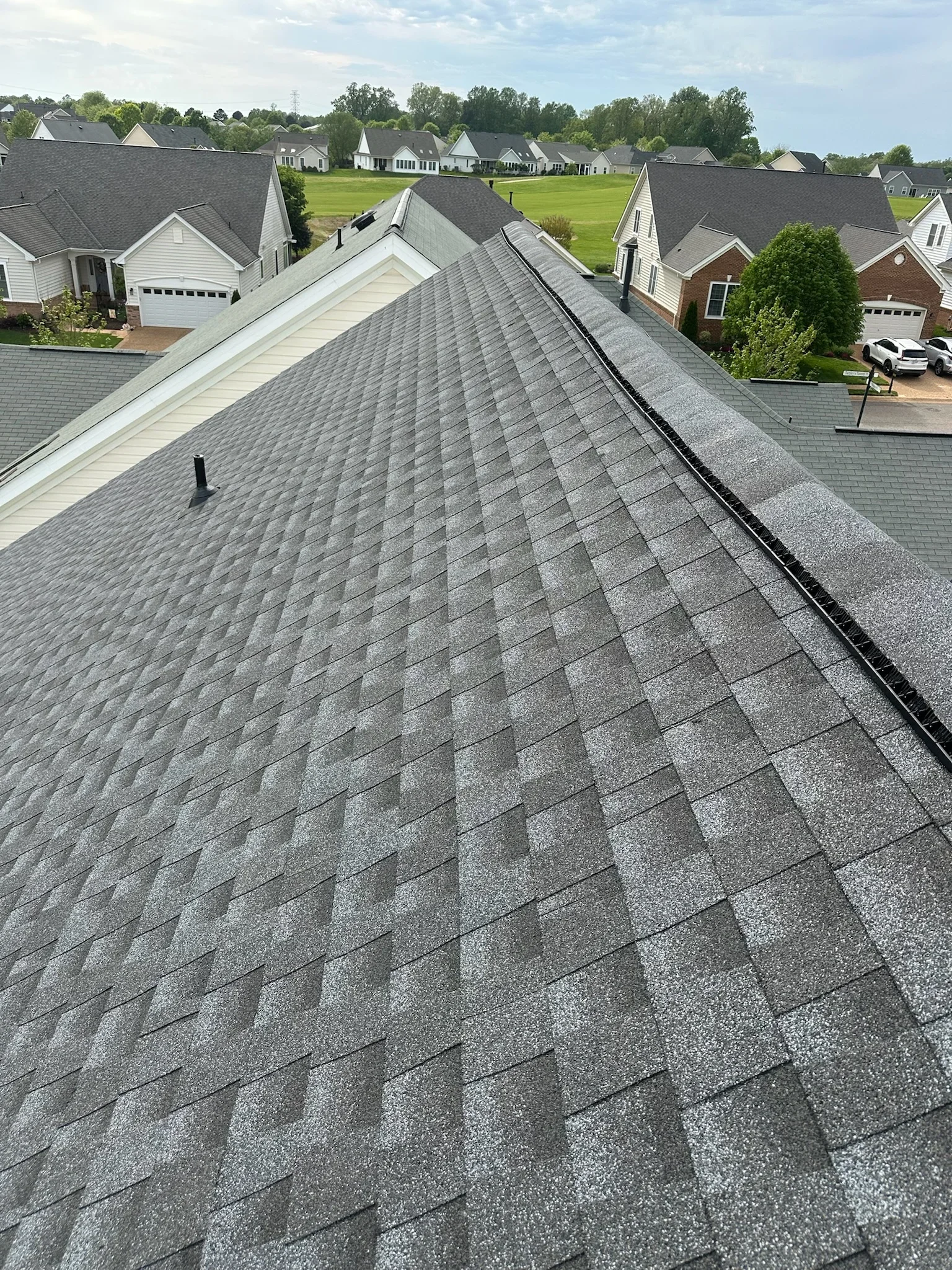 Charcoal gray architectural shingles installed on pitched residential roof with ridge cap and flashing