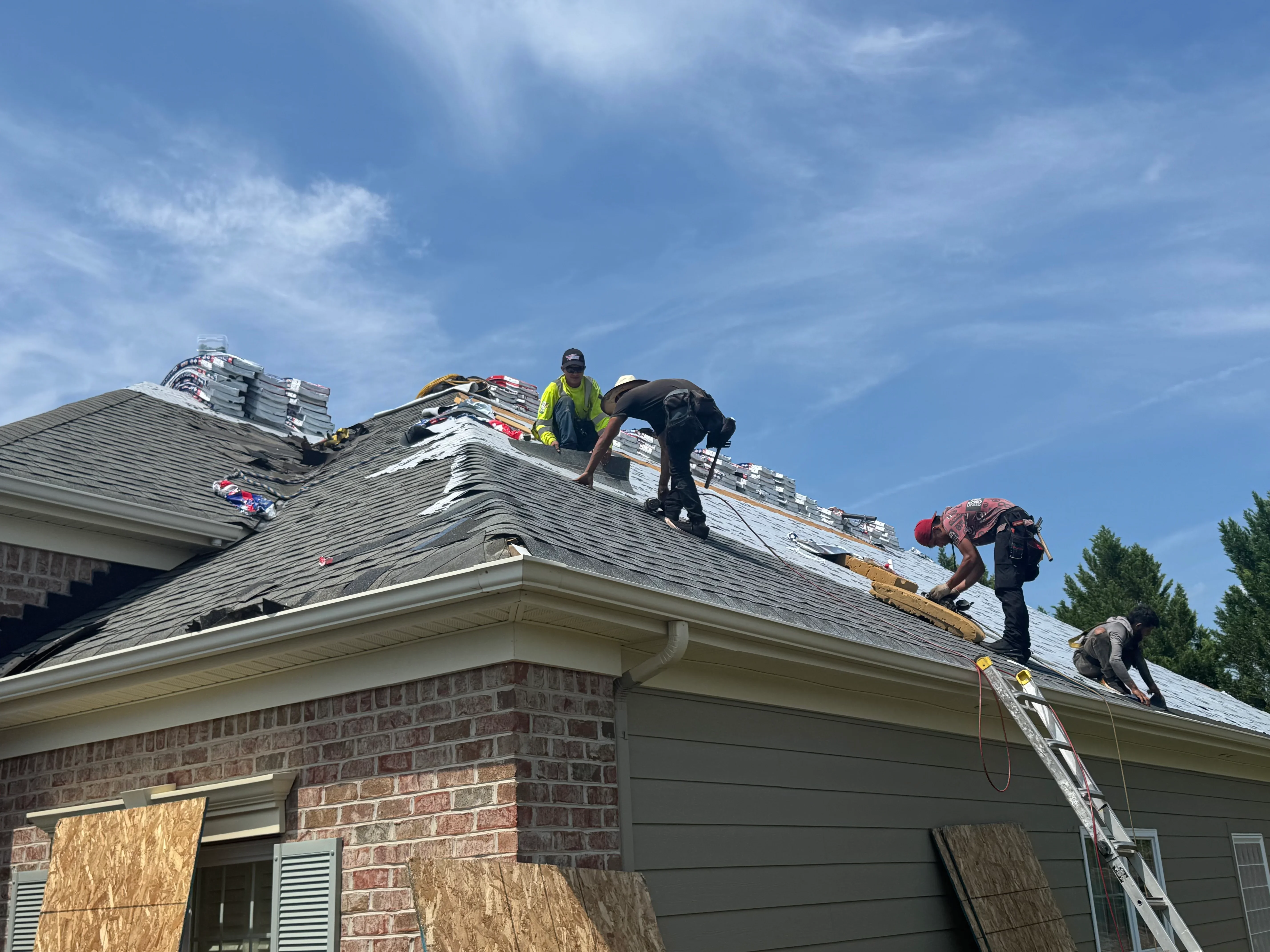 Roofing crew installing asphalt shingles on pitched residential roof with safety equipment