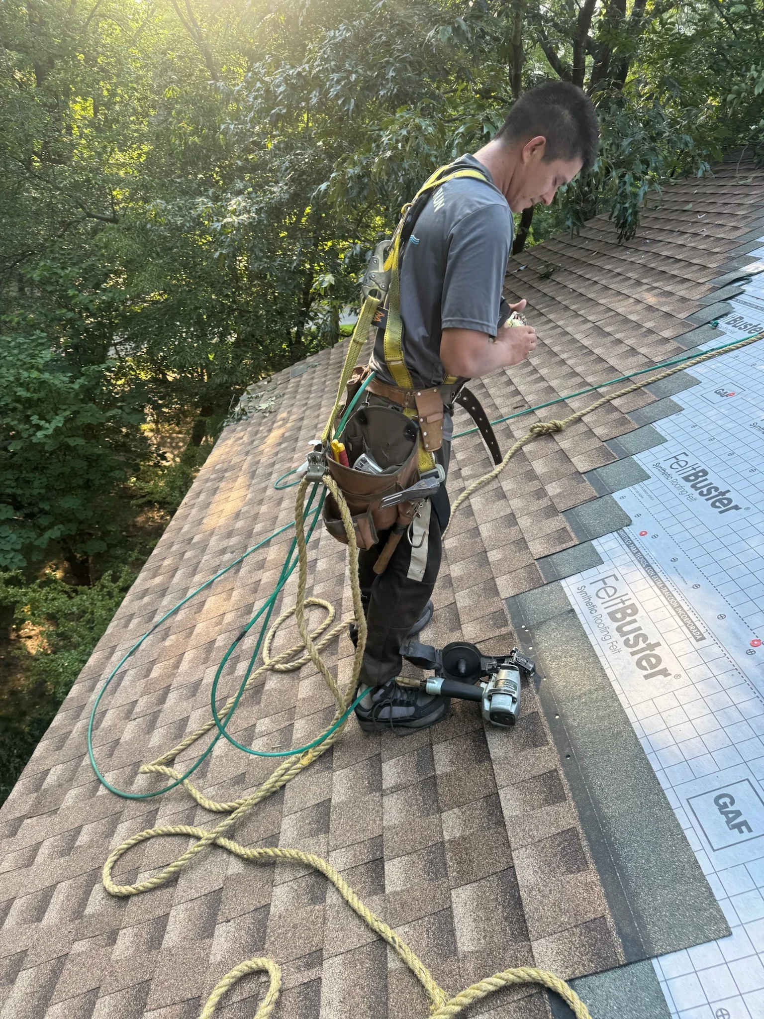 Roofer installing asphalt shingles with safety harness on pitched residential roof