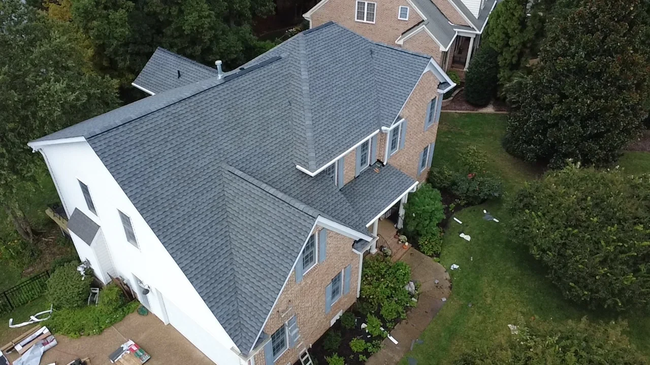 Aerial view of completed slate gray architectural shingle roof on brick home with white trim